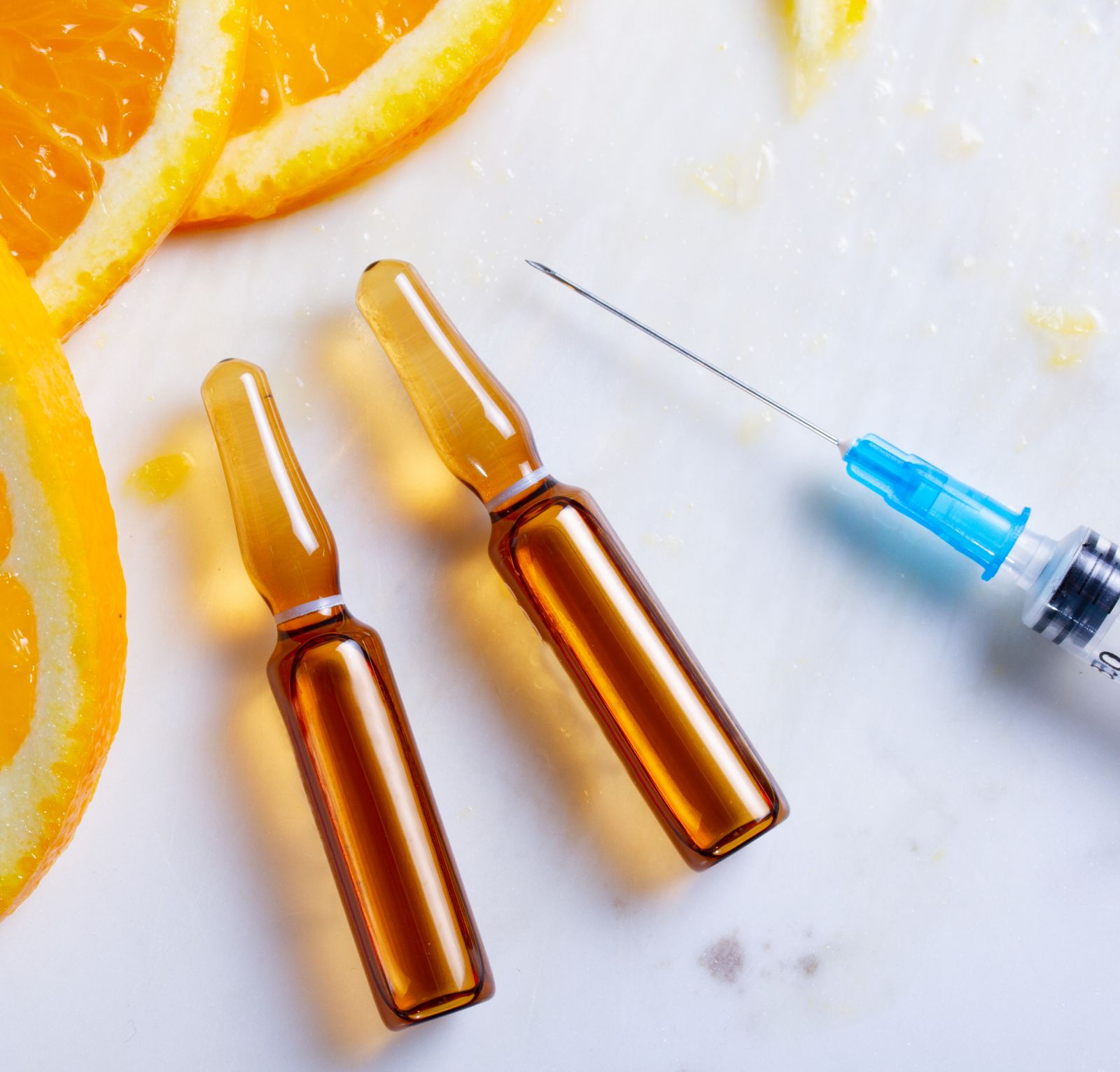 Two ampoules of orange juice next to a syringe.