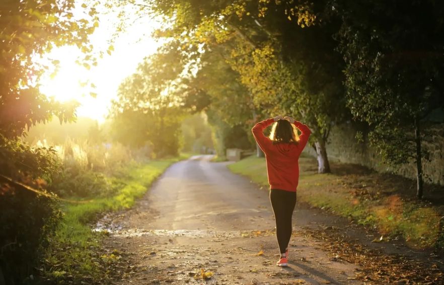 A woman is walking down the road in the sunlight.